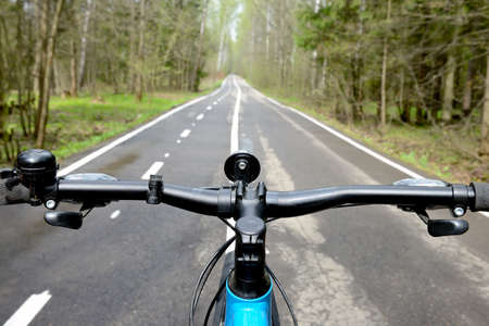 Bike on the bike path in the summer forest. View from the bike to the road going into the distance. Focus on the bike handlebar, blurred backgroundの写真素材