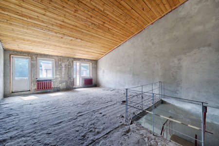 Empty living room in a country house without repair. Unfinished room with concrete walls and wooden beams on the ceilingの写真素材