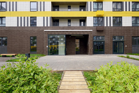 Typical modern entrance to the staircase of an apartment building. Path, lawn with plants in front of the entranceの写真素材