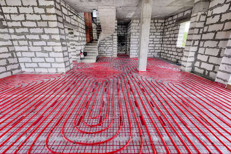 Installation of a heat flooring system in a country house under construction. Red tubes for floor heating. Modern heating system of a country houseの写真素材