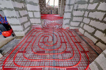 Installation of a heat flooring system in a country house under construction. Red tubes for floor heating. Modern heating system of a country houseの写真素材