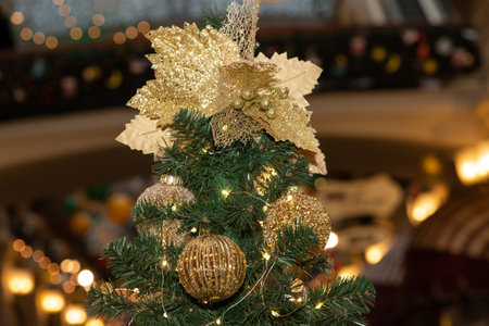 Golden Christmas balls and gold-colored leaves on a Christmas tree against the background of blurry lights of New Year's garlandsの写真素材