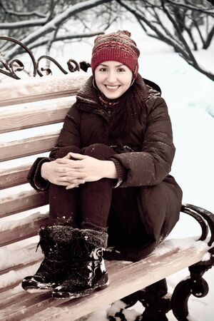 young woman in a red cap in winter park on a benchの写真素材
