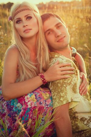 smiling young man and fine woman sit on meadow against sunset   style of hippieの写真素材