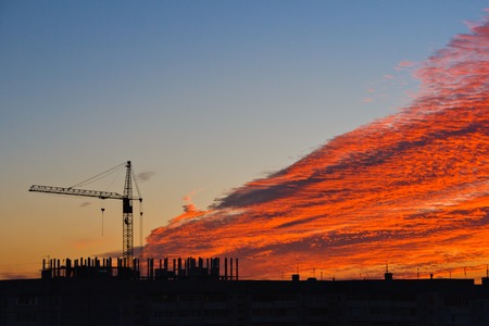 silhouette of construction crane and building on sunset sky background with red cloudsの写真素材