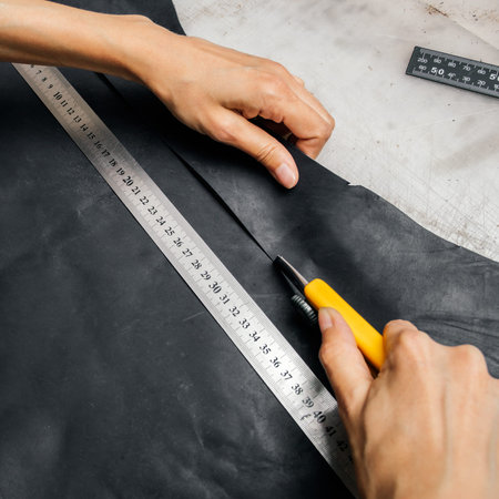 top view of a persons hands using cutting tool and metal ruler while producing leather goods