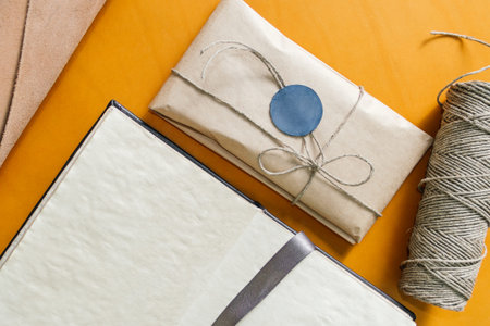 a notebook, a gift wrapped in paper with a seal, and a twine lie on yellow leather