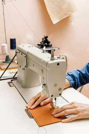 Side view of professional sewing machine in the workshop, womans hands hold a piece of yellow leatherの写真素材