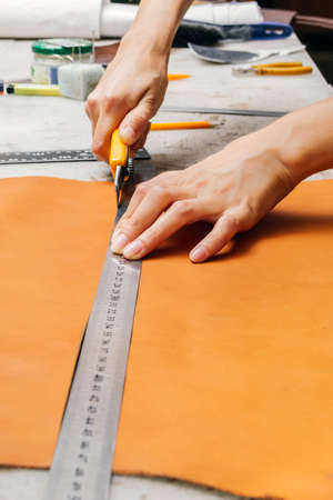 persons hands using cutting tool and metal ruler while producing leather goodsの写真素材