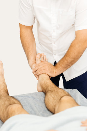 Osteopath working with ankle, examines a mans footの写真素材