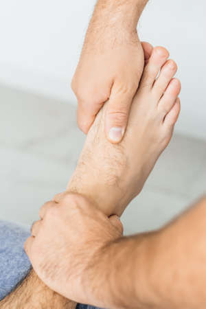 Osteopath working with ankle, examines a mans foot, close-upの写真素材