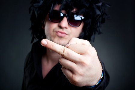 closeup picture of a man wearing a black feather wig, sunglasses, making a hand gesture