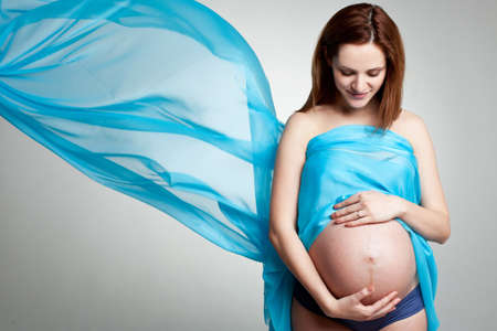 happy pregnant woman with blue material on the gray background の写真素材