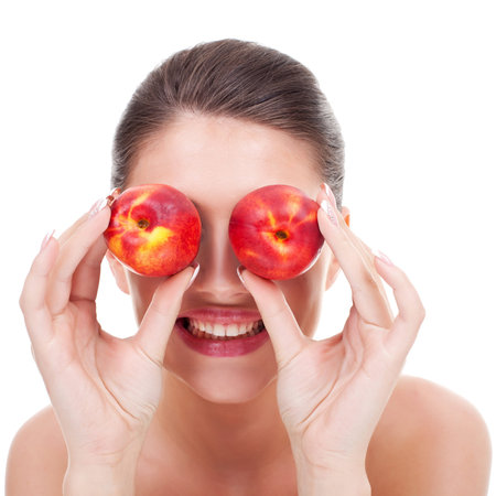 Young happy woman with red peaches over her eyes on white backgroundの写真素材
