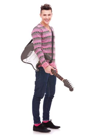 Rock star with an electric guitar isolated over white background . rock and roll image of a casual young man with a guitar on his shoulder, smiling to the cameraの写真素材