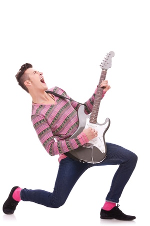 Rock star with a guitar screaming isolated over white background . rock and roll image of a young man playing an electric guitar and screaming. screaming young guitarist playing his guitarの写真素材