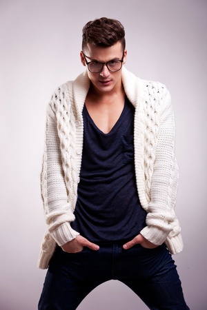 man wearing glasses and standing with hands in pockets on gray background. cool guy with hands in his pockets looking at the cameraの写真素材