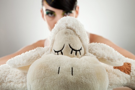 Young woman model behind her sheep toy and looking at the camera, over gray background.の写真素材
