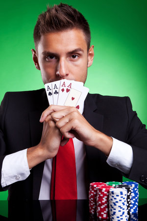 Young businessman card player covering his mouth with four aces, on green background