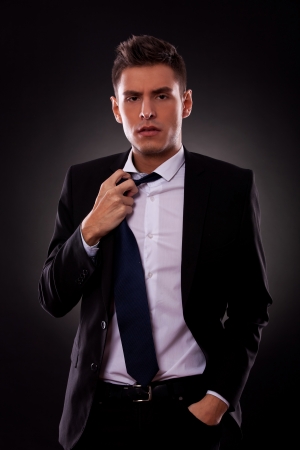 A Young businessman loosing his tie. on black backgroundの写真素材