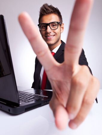 Happy young business man showing victory gesture at office desk , smiling. の写真素材