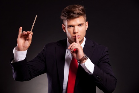young business man posing as a conductor who makes silence with his finger on his lips, on dark backgroundの写真素材