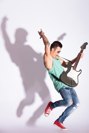 full length photo of a young casual fashion man practicing his rock on an electric guitar, against gray background and hard shadowの写真素材