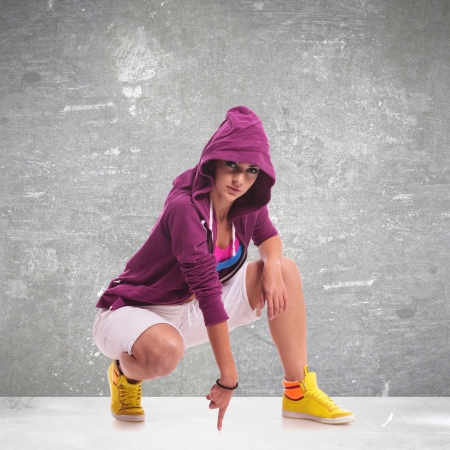 young hip hop woman dancer wearing a hoodie, posing crouched and touching the floorの写真素材