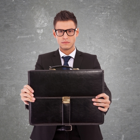 serious business man wearing glasses, offering a briefcase to you on gray backgroundの写真素材