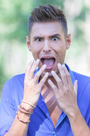 closeup portrait of a young casual man shouting out of horror in a parkの写真素材