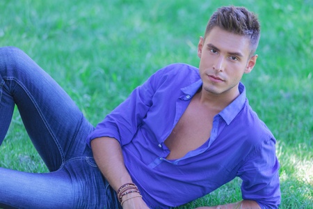 young casual man resting in the grass and looking at the cameraの写真素材