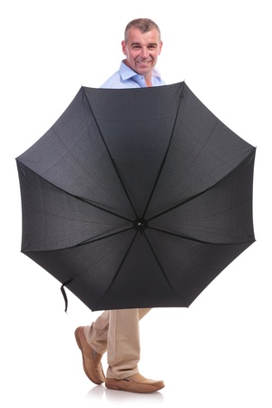 casual senior man smiling from behind his opened umbrella. isolated on white backgroundの写真素材