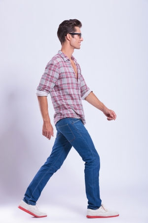 full length picture of a casual young man walking to the side of the camera and looking forward. on gray backgroundの写真素材