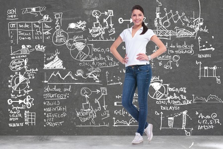full length picture of a young casual woman standing with her hands on her hips in front of a background full of sketches and charts and smiling for the cameraの写真素材