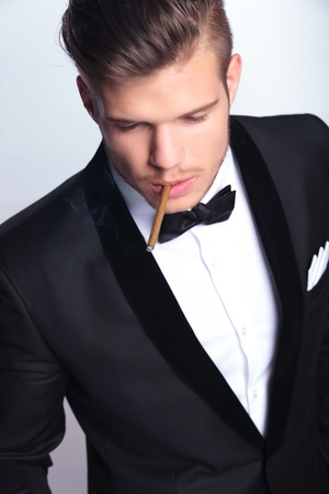 cutout picture of an elegant young fashion man in tuxedo smoking while looking away from the camera. on gray backgroundの写真素材