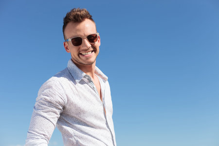 casual young man outdoor smiling to the camera with a blue sky behindの写真素材