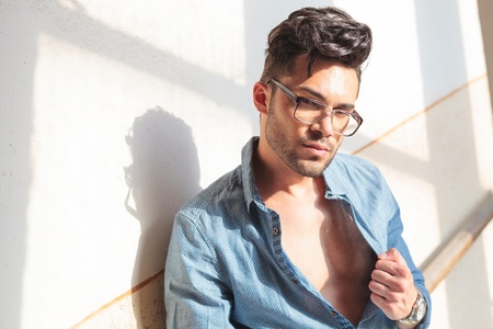 casual young man posing in a staircase with an unbutonned shirt and the sun shining on him while he looks at the cameraの写真素材