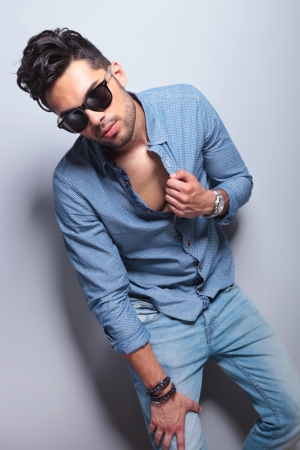 casual young man with a hand on his leg and the other on his unbuttoned shirt while looking at the camera. on gray backgroundの写真素材