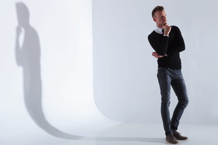 full length picture of a pensive casual young man looking away from the camera while holding his...