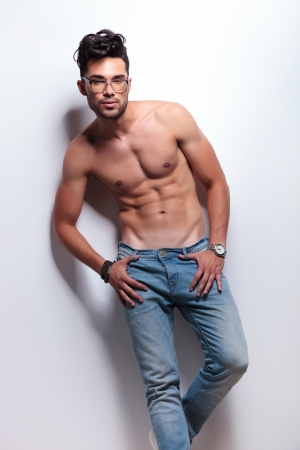 young topless man standing with his thumbs in the loops of his jeans and looking at the camera. on light gray backgroundの写真素材