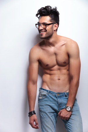 young topless man holding a hand on his crotch while looking away from the camera and smiling. on light gray backgroundの写真素材