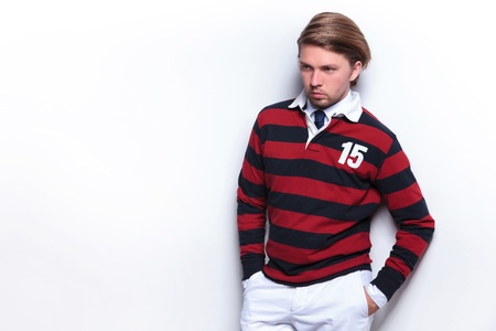 picture of a young casual man holding his hands in his pockets while looking away from the camera and leaning on a wall. on light gray backgroundの写真素材