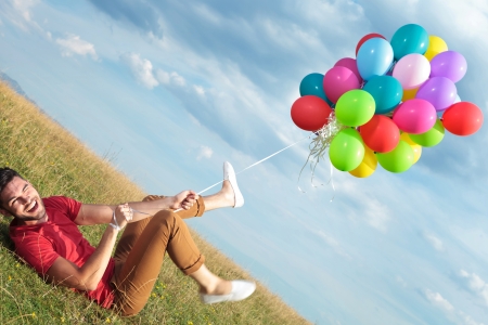 casual young man being pulled up by balloons outdoorの写真素材
