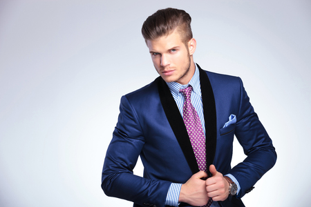 closeup of a young business man holding his hands on his suit jacket while looking into the camera. on a gray backgroundの写真素材