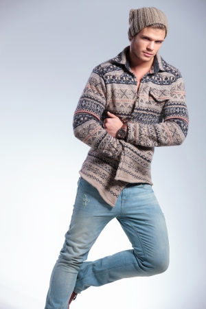 casual young man standing in one leg and a hand tucked in his jacket while looking at the camera. on gray backgroundの写真素材