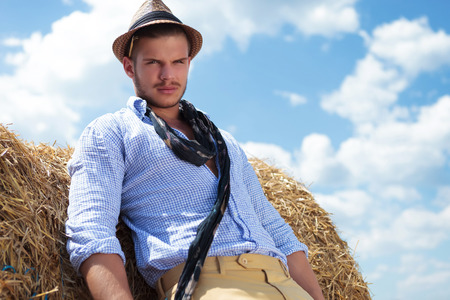 young casual man posing outdoor and looking into the camera while leaning on a haystackの写真素材