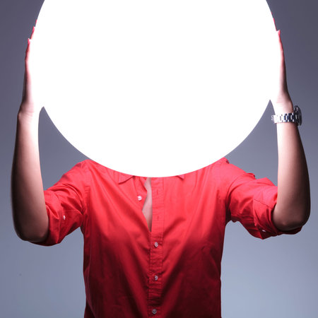 young casual woman covering her ears over a shiny blank circle. hear no evil concept. on gray...