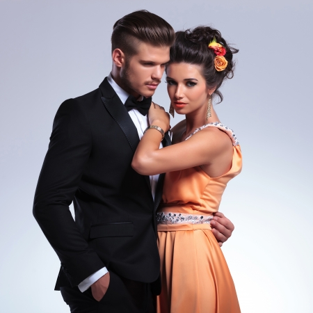 closeup portrait of a young fashion couple embracing while the woman is looking at the camera and the man is holding a hand in his pocket. on gray backgroundの写真素材