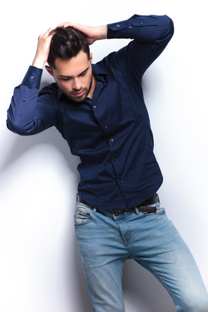 young fashion man holding both hands in his hair while looking down, away from the camera. on a light backgroundの写真素材
