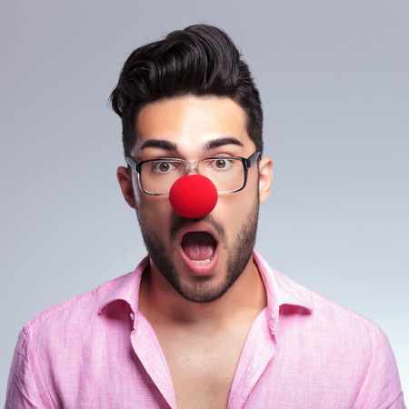 closeup portrait of a young fashion man with a red nose being shocked and looking at the camera with his mouth wide opened. on a light backgroundの写真素材